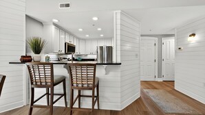 A modern kitchen with white cabinetry, a central island, and two bar stools.