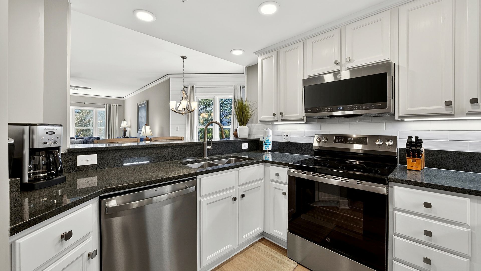 A modern kitchen with white cabinetry, stainless steel appliances, and a black granite countertop.
