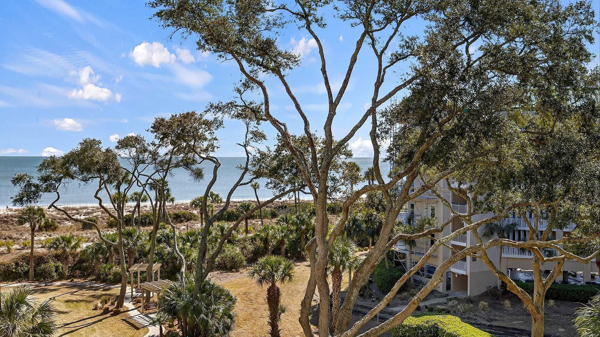 Vista costera con árboles, una playa y un edificio con balcones.