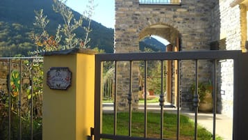 A gated entrance with a stone building in the background, a sign with "Agrade" on it, and a mountain in the distance.
