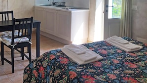 A compact room with a bed, a desk, a chair, a kitchenette, and a window with curtains. - Agriturismo Mamma Chica (La Spezia)