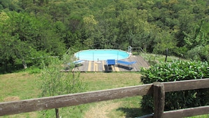 A wooden deck with a pool and lounge chairs, surrounded by lush greenery and hills. - Agriturismo Mamma Chica (La Spezia)