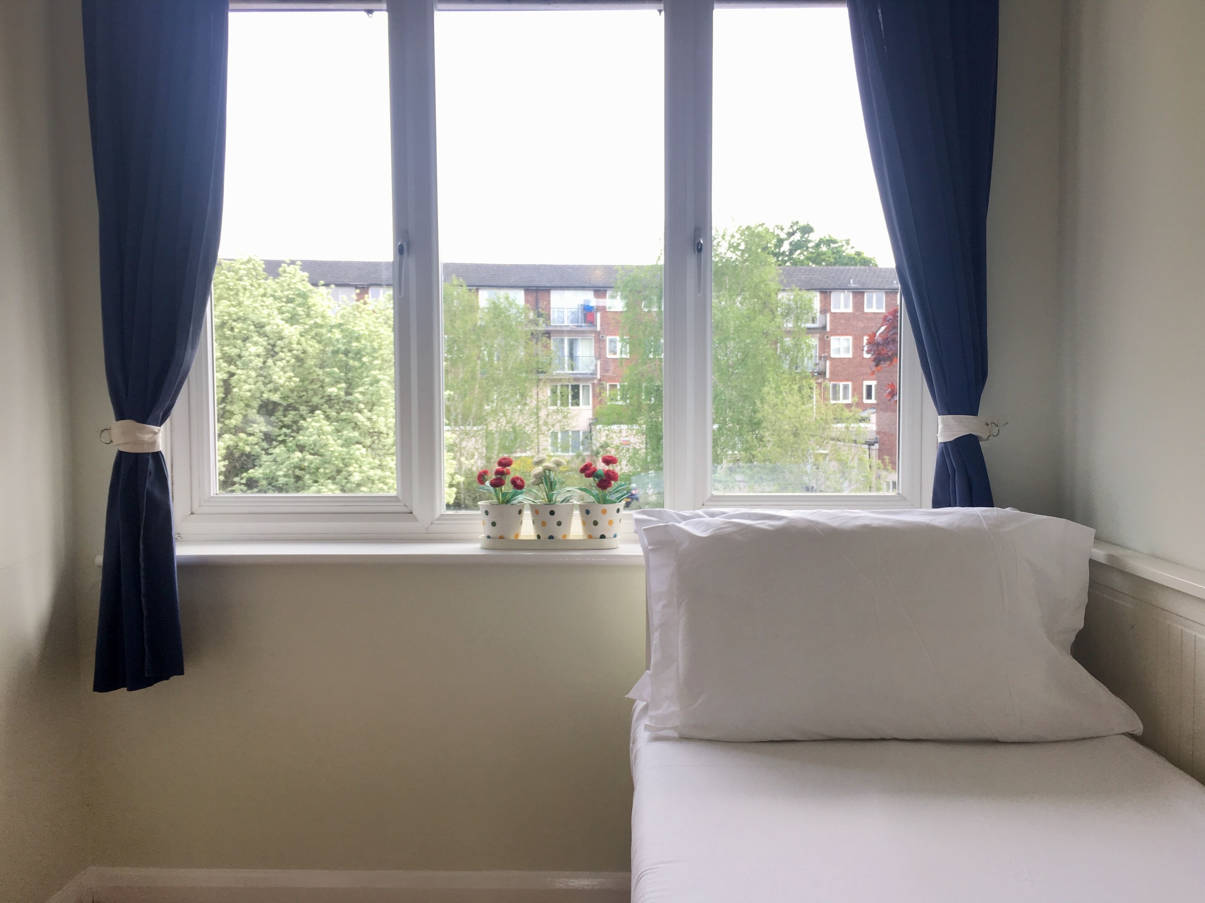 Una camera da letto con un letto, una finestra con tende e vista su edifici e alberi.