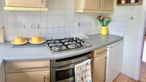 A kitchen with a gas stove, oven, and a yellow vase with flowers on the counter. - Apple Perch 2BR Flat-Free Parking (Oxford)