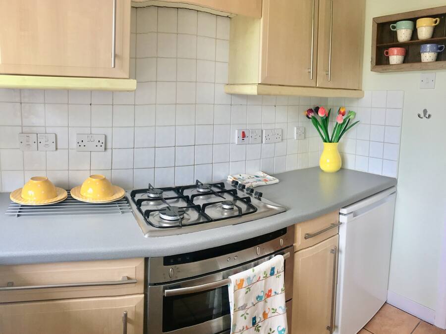 A kitchen with a gas stove, oven, and a yellow vase with flowers on the counter.