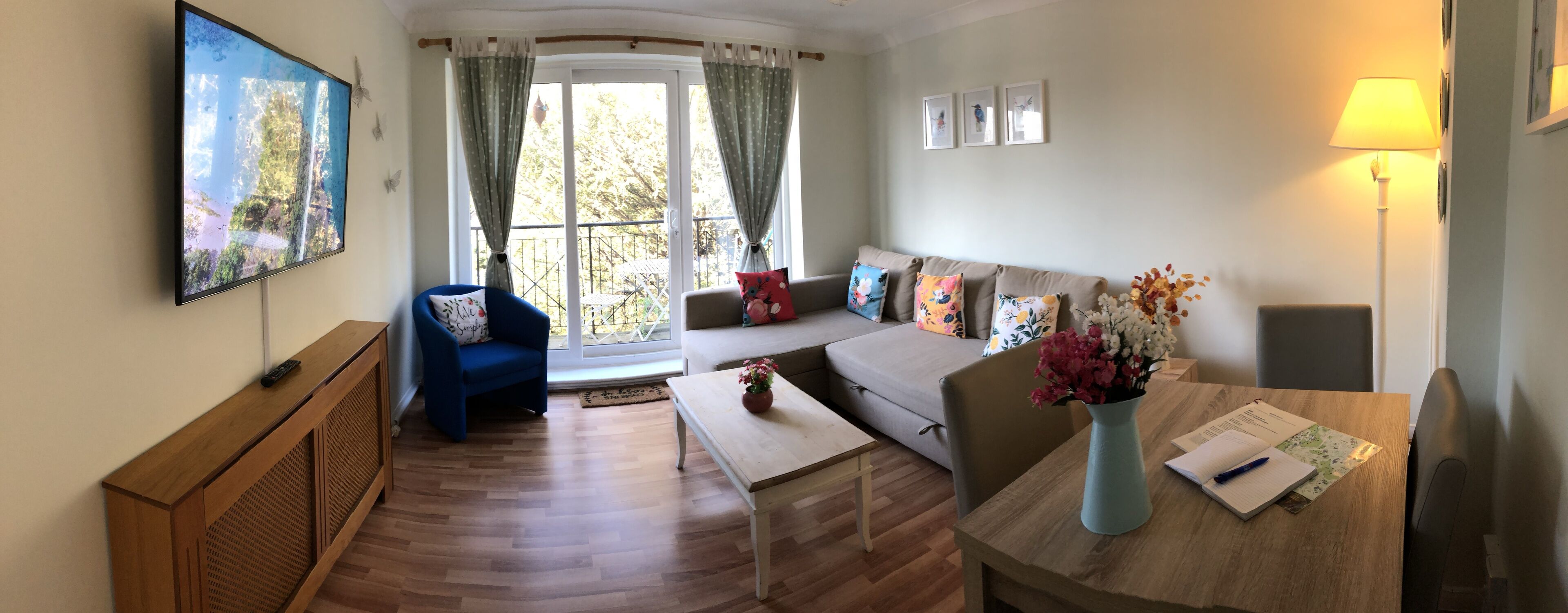 A living room with a sofa, a blue armchair, a coffee table, a TV, and a window with curtains.