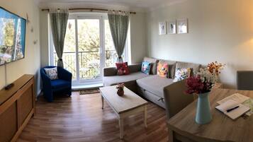 A living room with a sofa, a blue armchair, a coffee table, a TV, and a window with curtains.