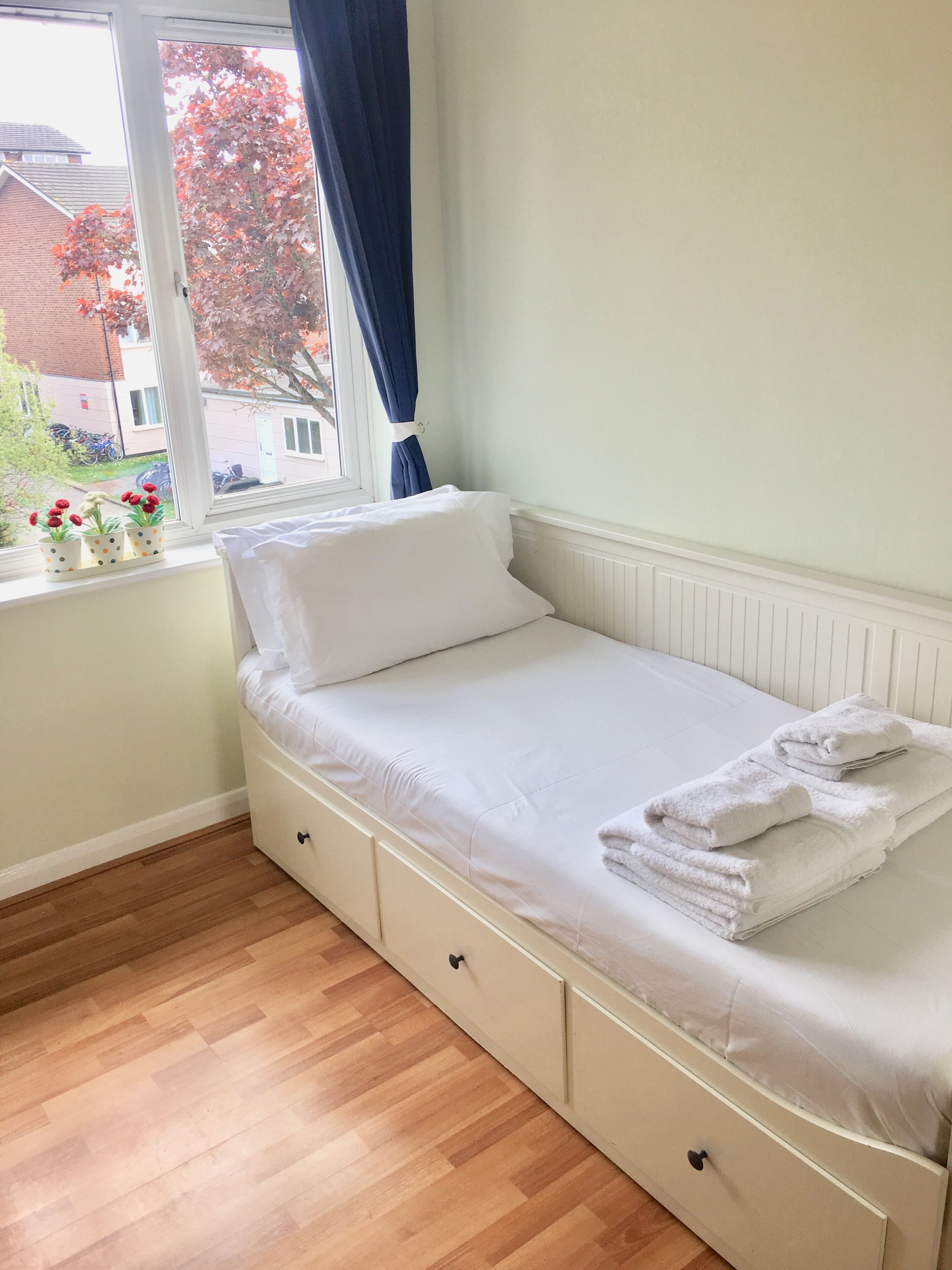 A small, single-bed room with a window, wooden flooring, and a view of the outside.