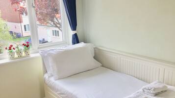 A small, single-bed room with a window, wooden flooring, and a view of the outside.