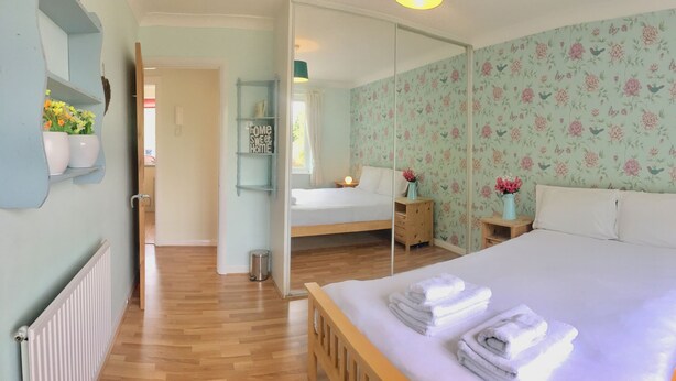 A bedroom with a bed, bedside tables, a mirror, a window with flowers, and a floral wallpaper. - Apple Perch 2BR Flat-Free Parking (Oxford)