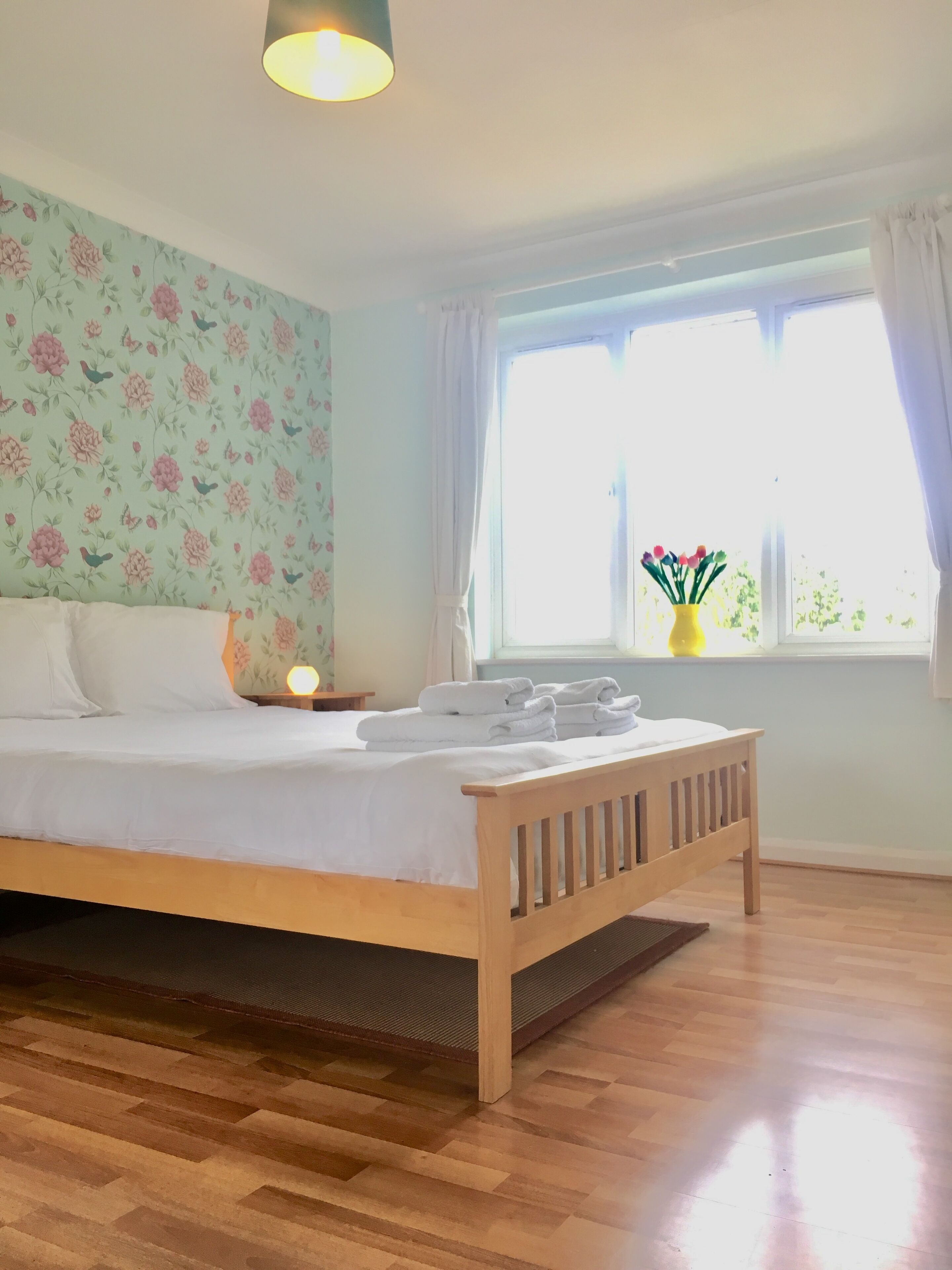 A neatly made bed with white linens, a wooden headboard, and a bedside table with a lamp.