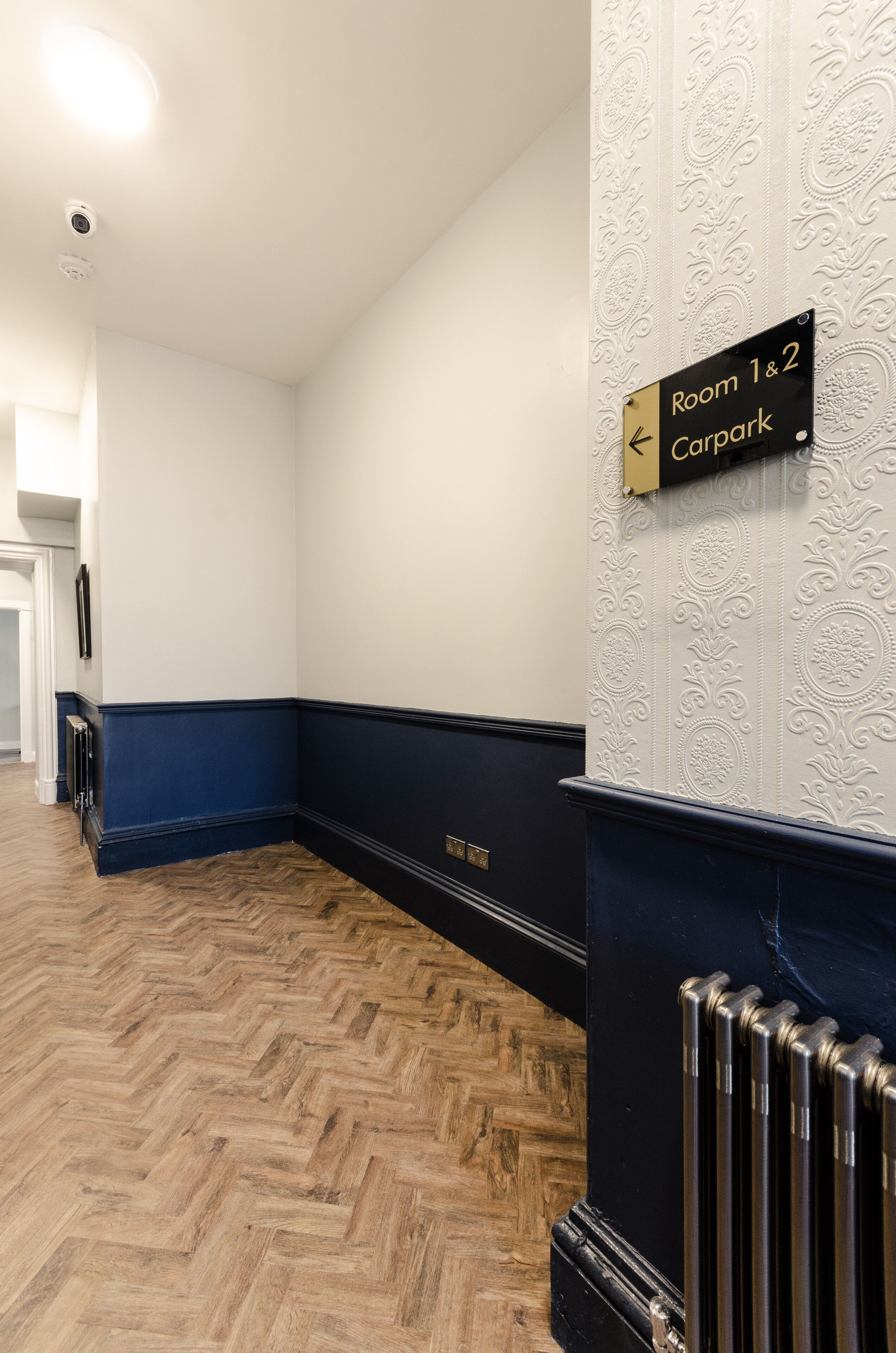 A hallway with a sign indicating 'Room 1 & 2 Carpark' and a direction arrow.