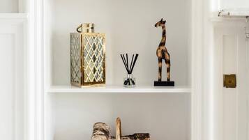 A white shelf with a clock, a decorative box, a reed diffuser, a giraffe figurine, and a wicker basket.