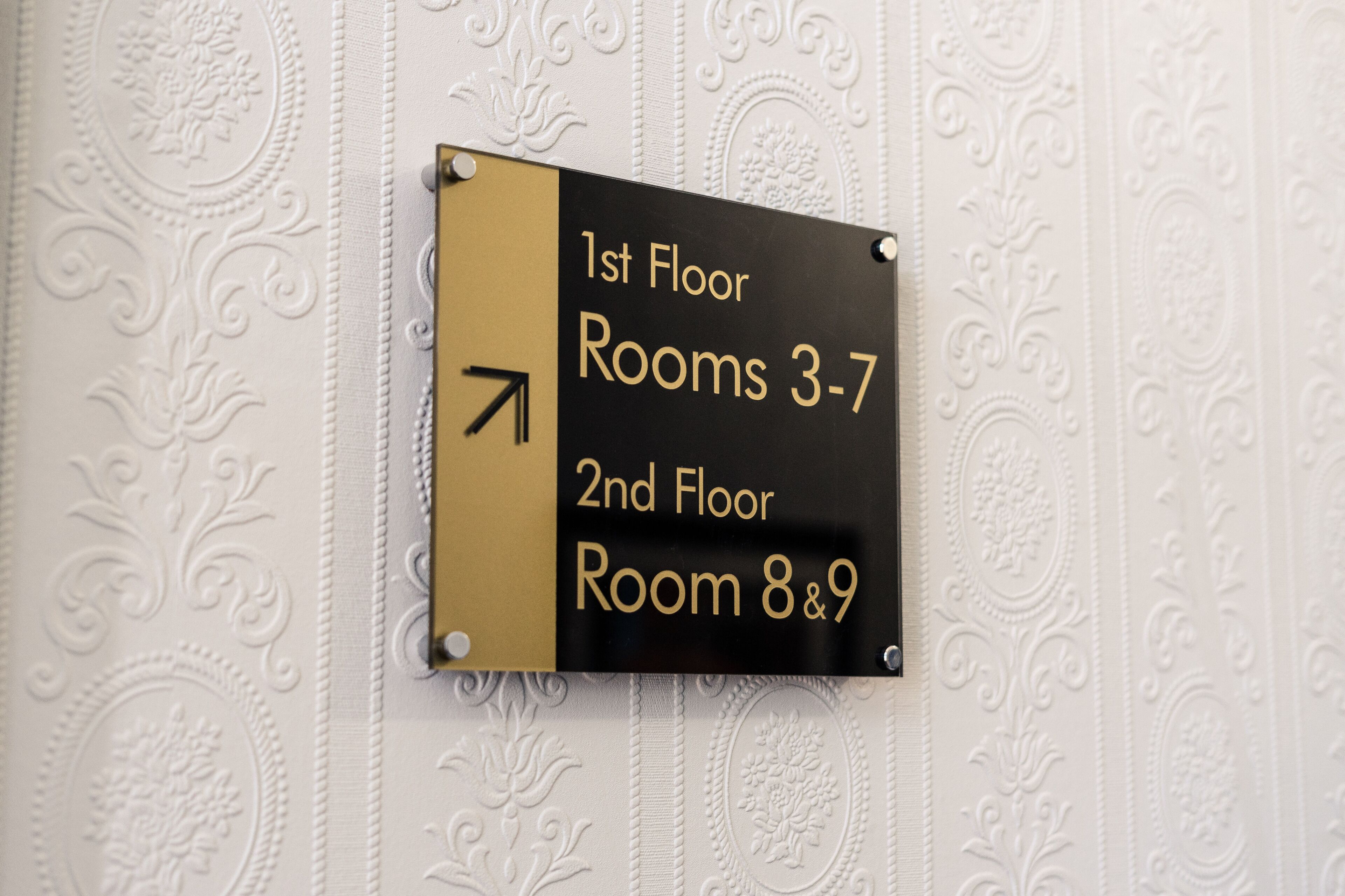 Placa de direção indicando quartos do 1º andar, de 3 a 7, e quartos do 2º andar, 8 e 9.