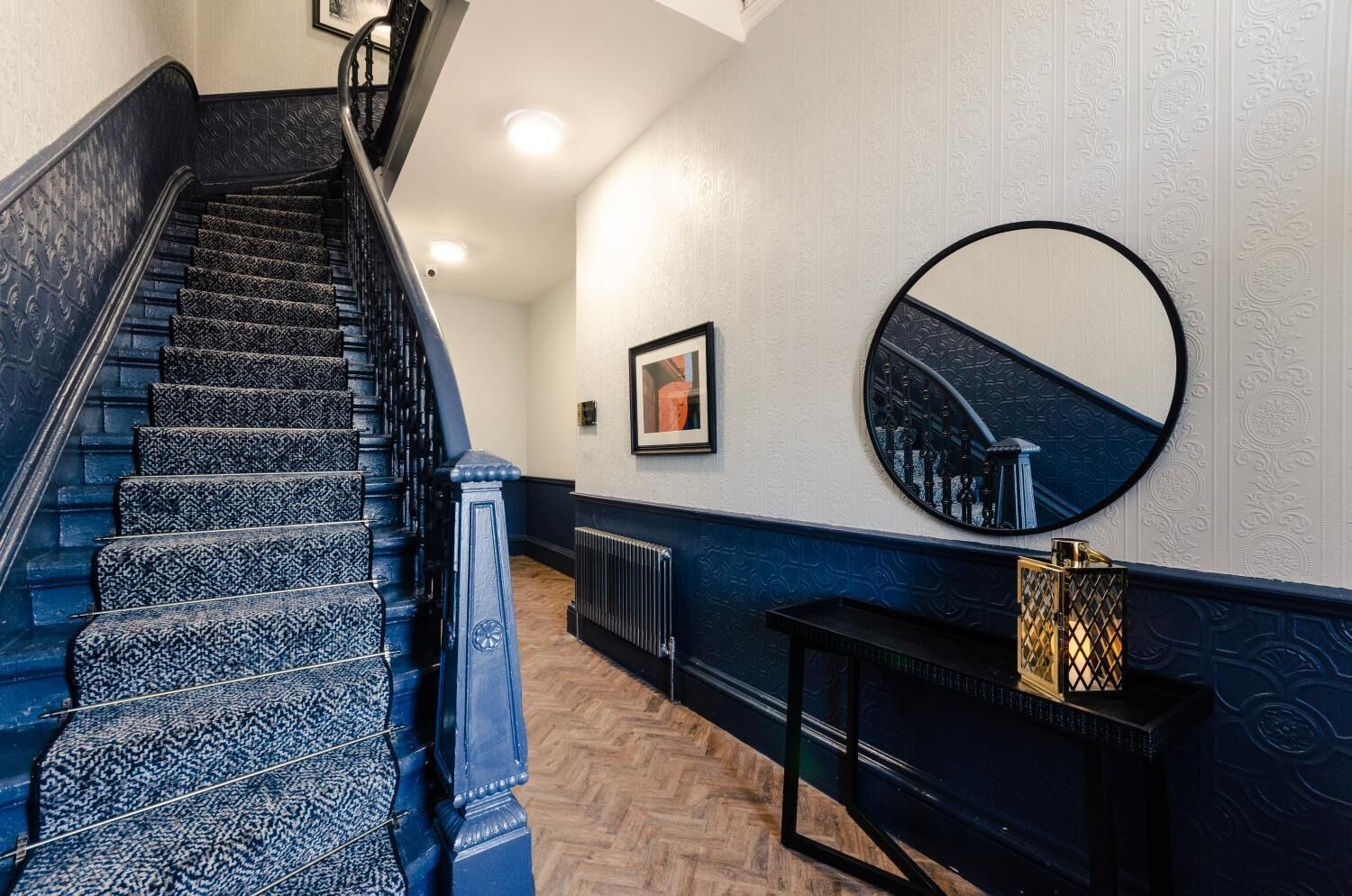 A staircase with patterned carpet, a black console table with a mirror, and a radiator on the wall.