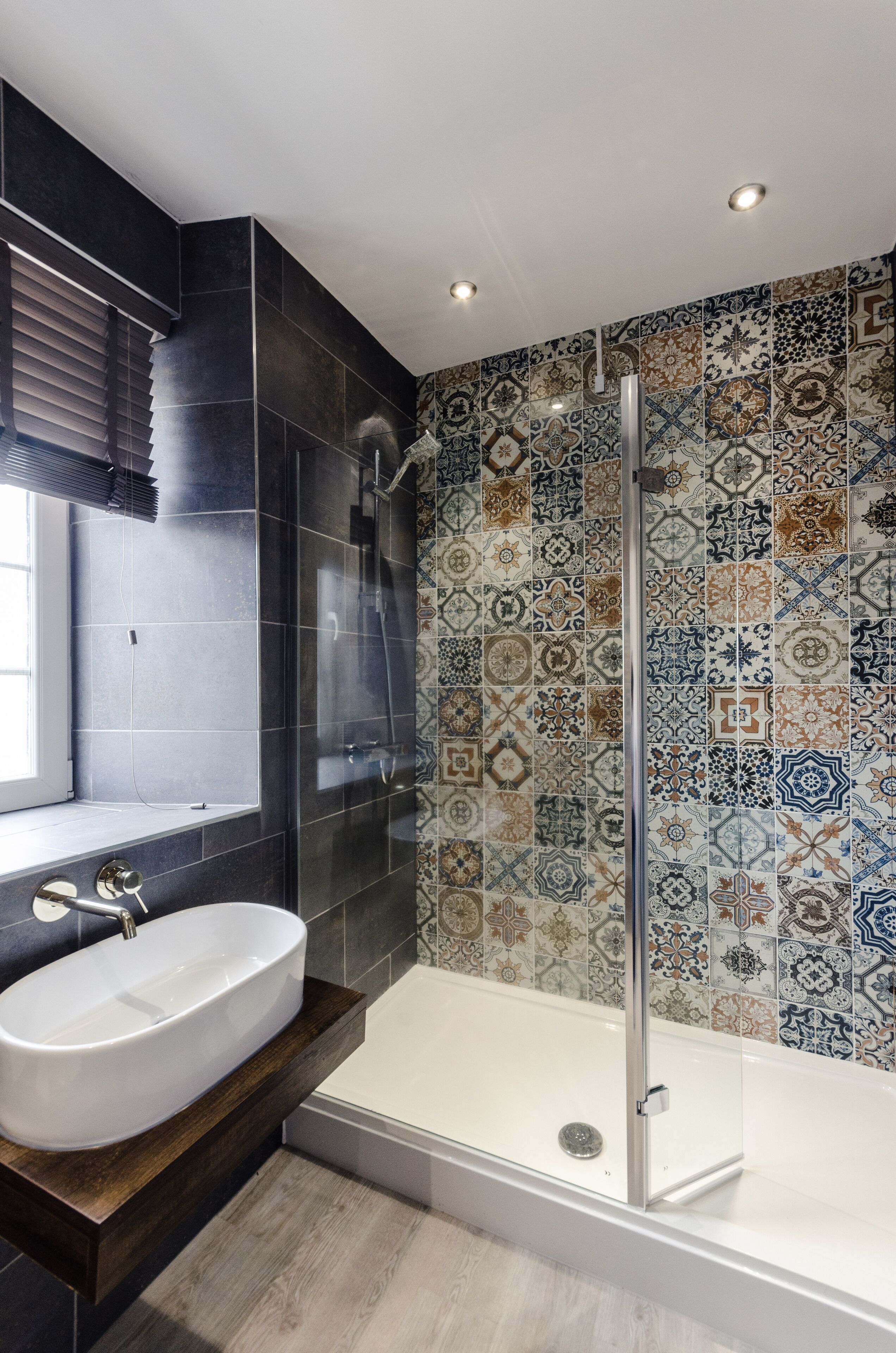 Un bagno moderno con un ampio lavandino bianco, una doccia vetrata e un muro rivestito di piastrelle con un motivo geometrico.