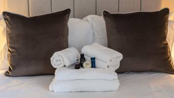 Una cama bien hecha con dos almohadas marrones, una pila de toallas blancas y una botella de loción.