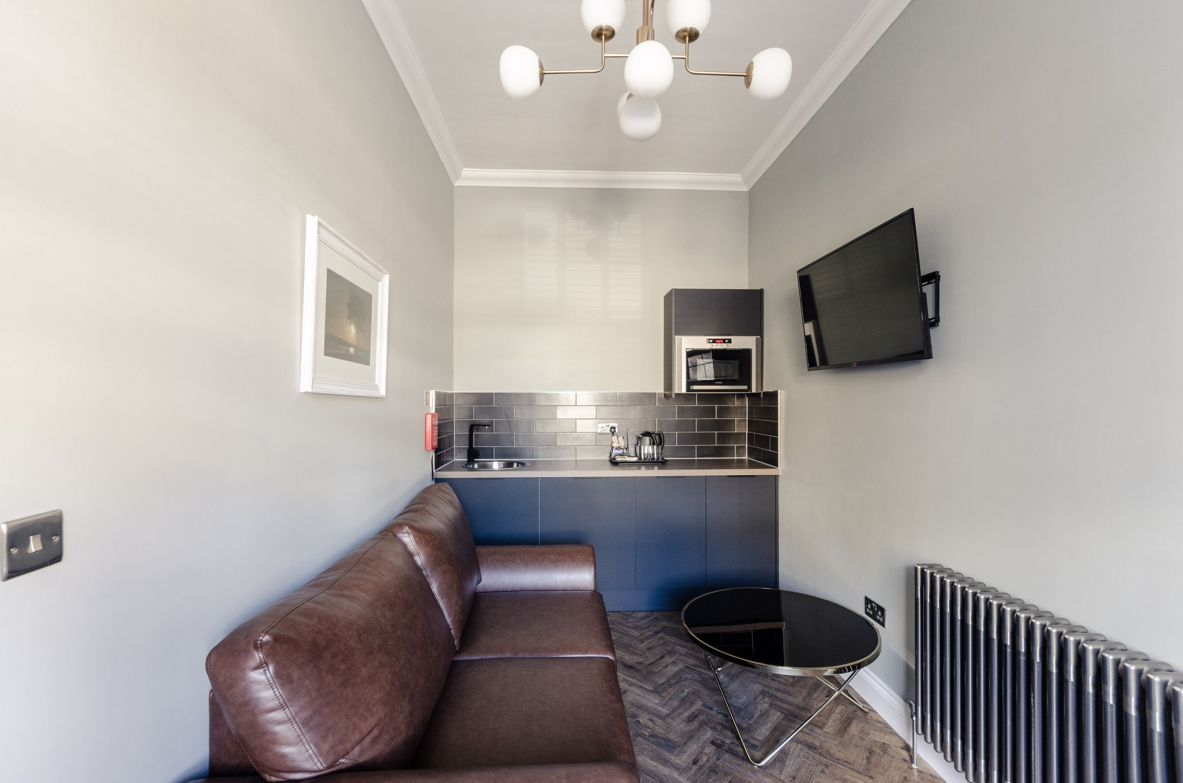 A modern kitchen with a built-in oven and microwave, a brown leather sofa, and a small round table.