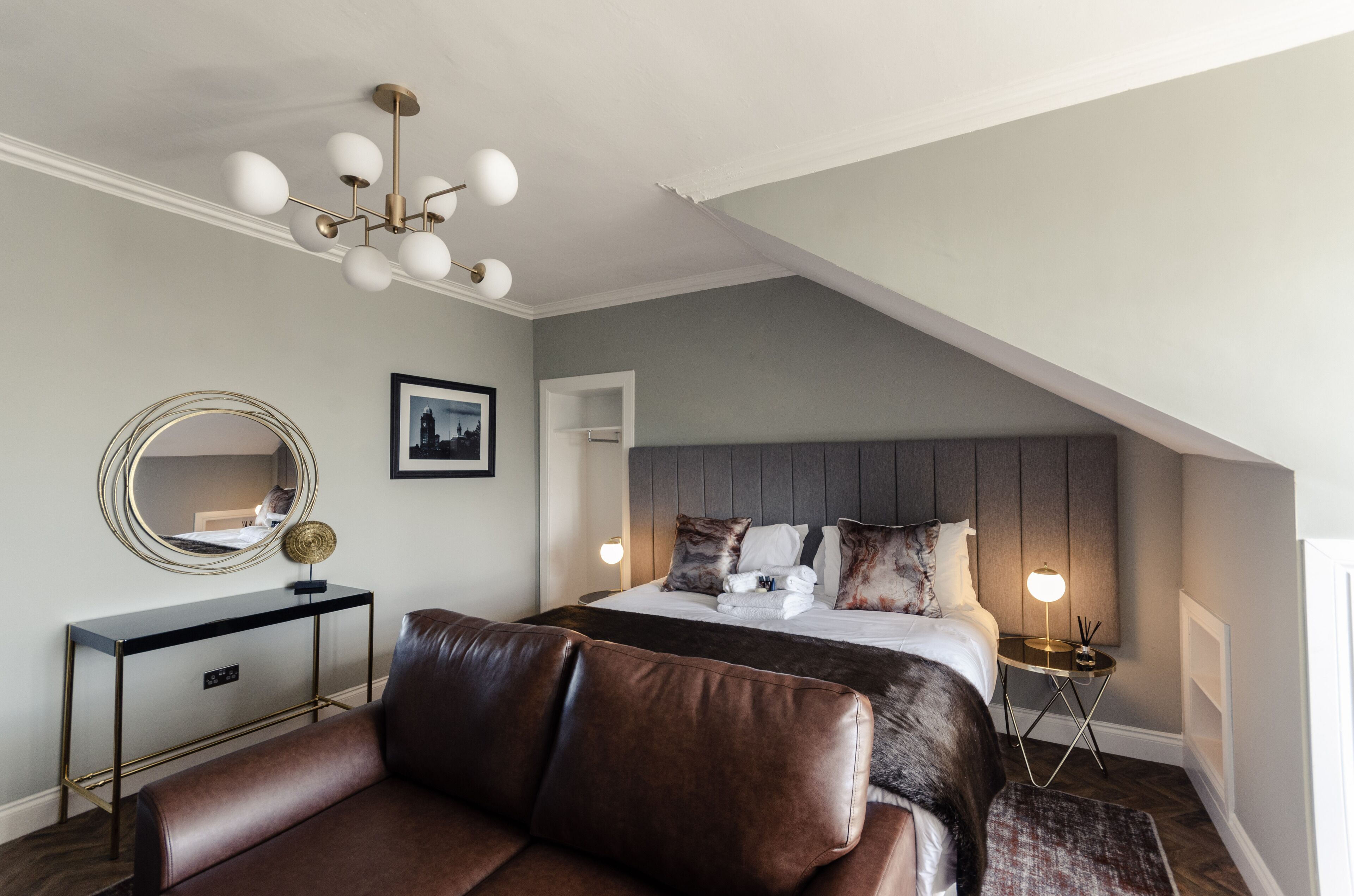 A modern bedroom with a large bed, a leather sofa, a console table, and a unique ceiling light fixture.
