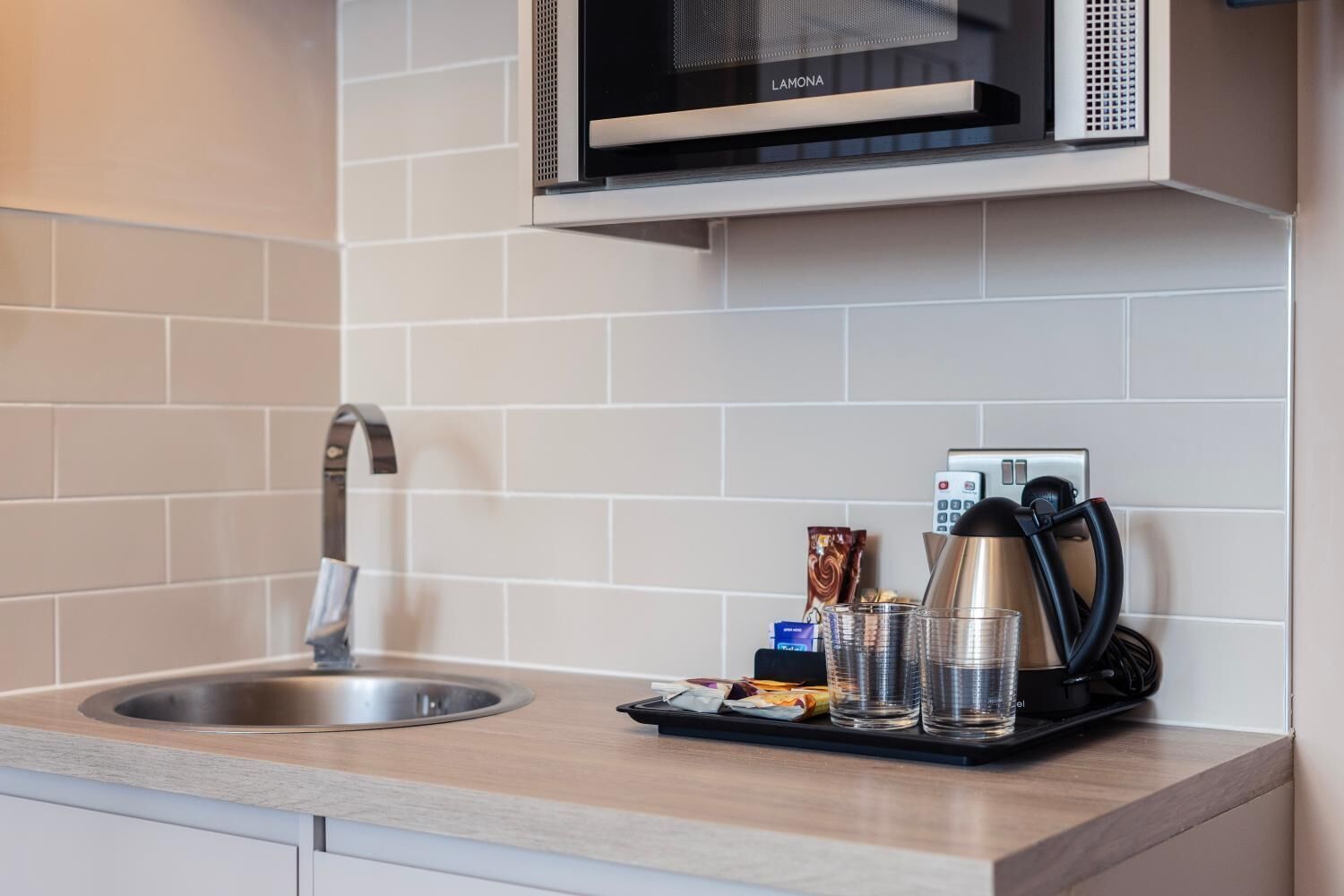 A modern kitchen with a stainless steel sink, a microwave, a coffee machine, and a kettle on the counter.