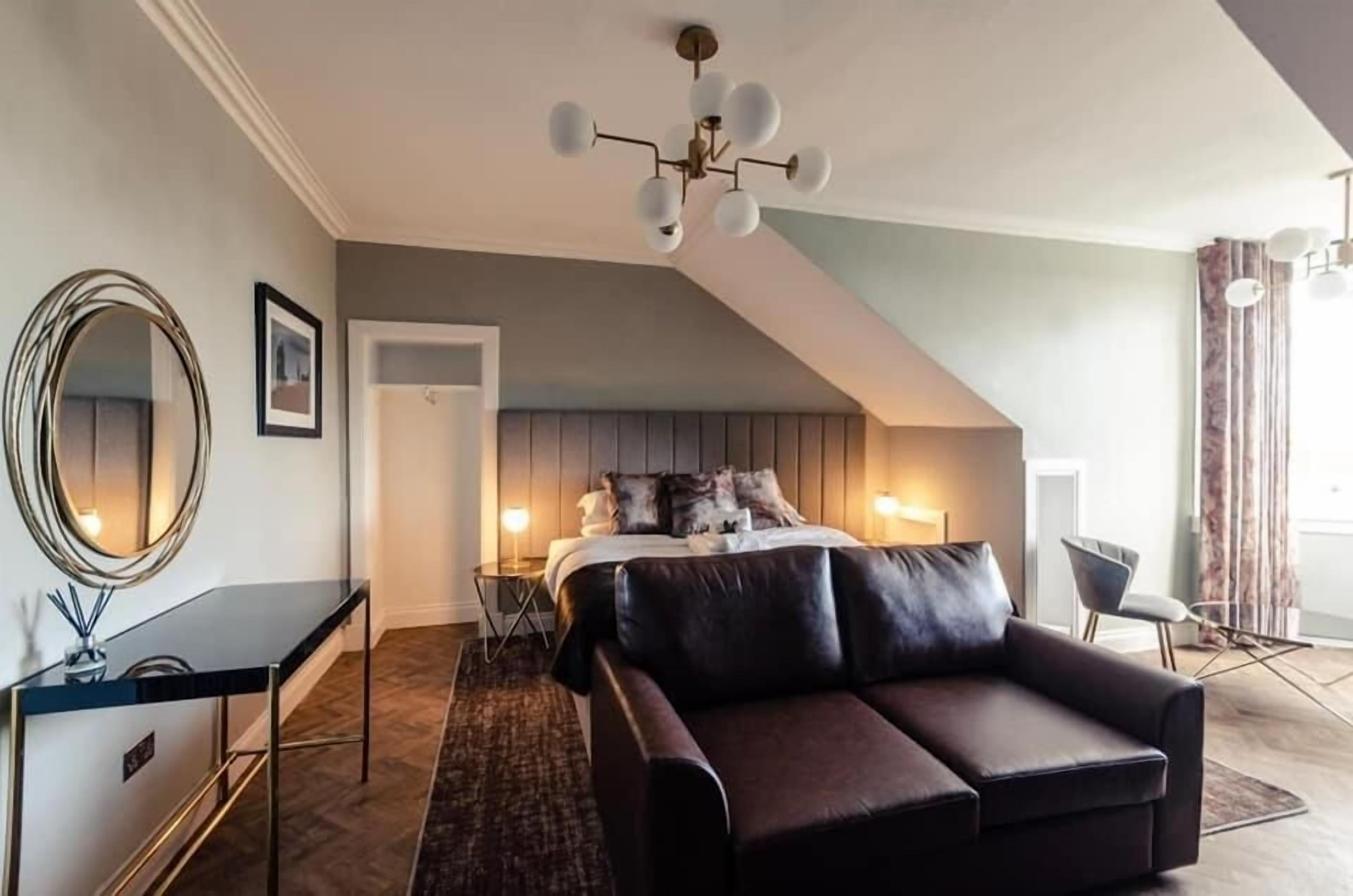 A modern bedroom with a large bed, a dark leather sofa, a round mirror, and a desk.