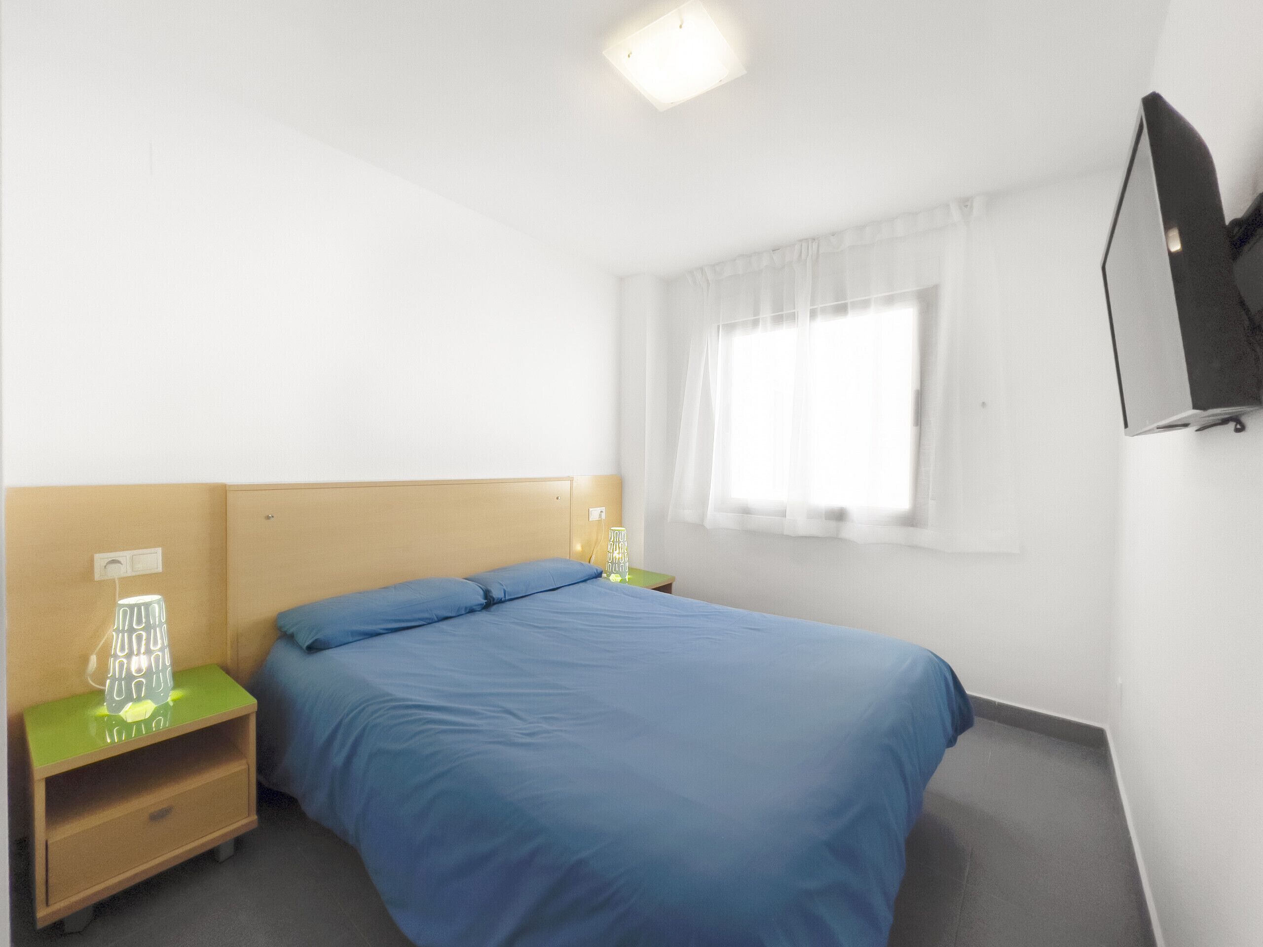 A hotel room with a bed, a nightstand, a TV, and a window with curtains.