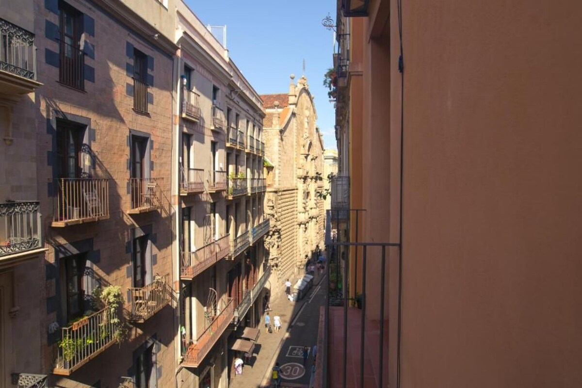 Une rue étroite, bordée de bâtiments des deux côtés, avec des balcons et un ciel d’un bleu éclatant.