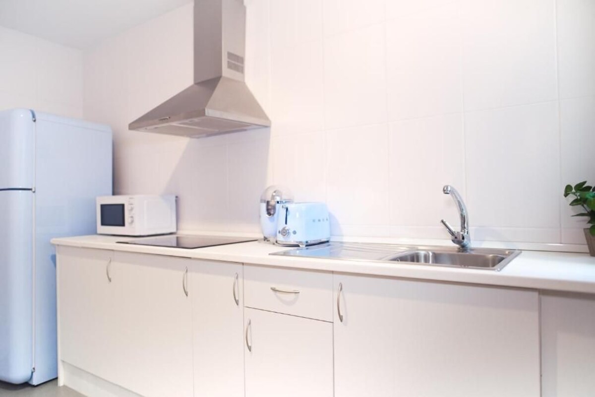 Une cuisine moderne avec des armoires blanches, un évier en acier inoxydable, un four à micro-ondes et un grille-pain.