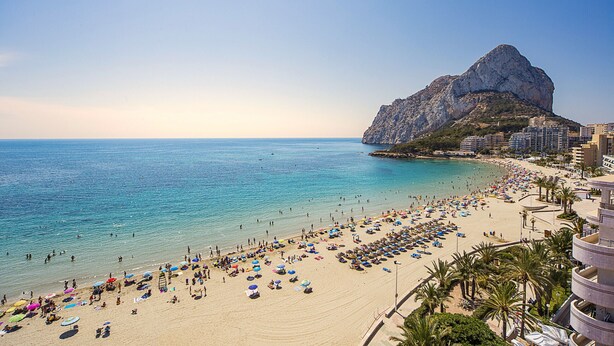 A beach with a large rock formation, clear blue water, and numerous beach umbrellas. - First line / Wifi / Spa / Seaviews / Heated pool / Pets (Calpe)
