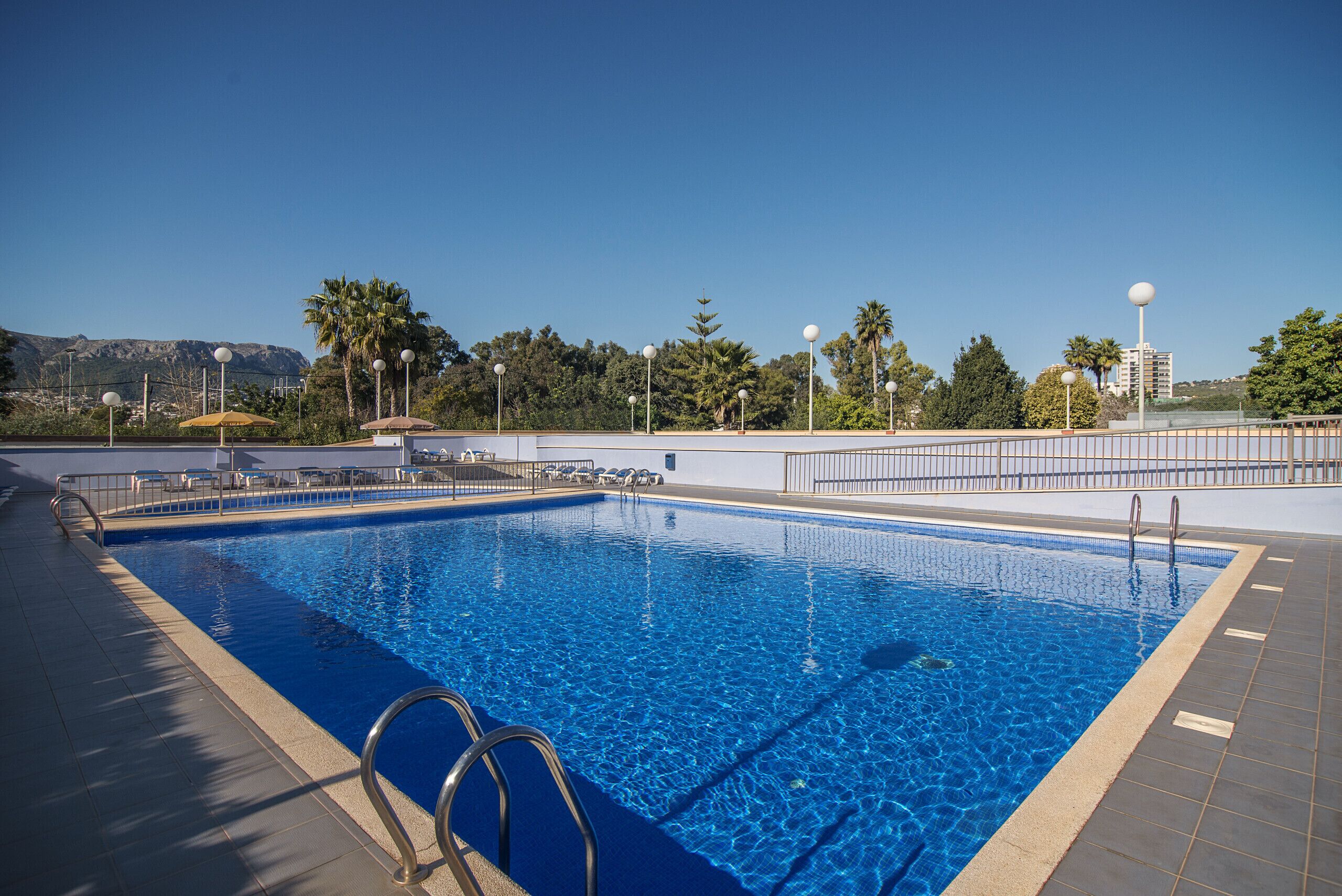 A rectangular swimming pool with clear blue water, surrounded by a tiled deck and metal railings.