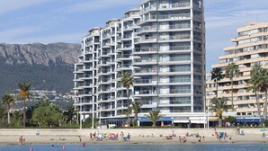 A multi-story hotel with balconies, located near a beach with palm trees and a mountainous backdrop. - First line / Wifi / Spa / Seaviews / Heated pool / Pets (Calpe)