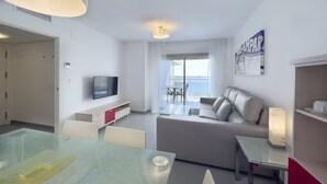 A modern living room with a sofa, a TV, a dining table, and a balcony with a view of the sea. - First line / Wifi / Spa / Seaviews / Heated pool / Pets (Calpe)