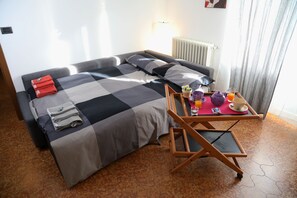 Une chambre d’hôtel avec un canapé-lit, une petite table avec des articles pour le petit-déjeuner et un radiateur.