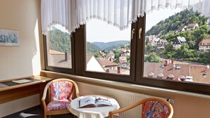 A room with a view of a hillside village through large windows, a table with an open book, and two chairs.