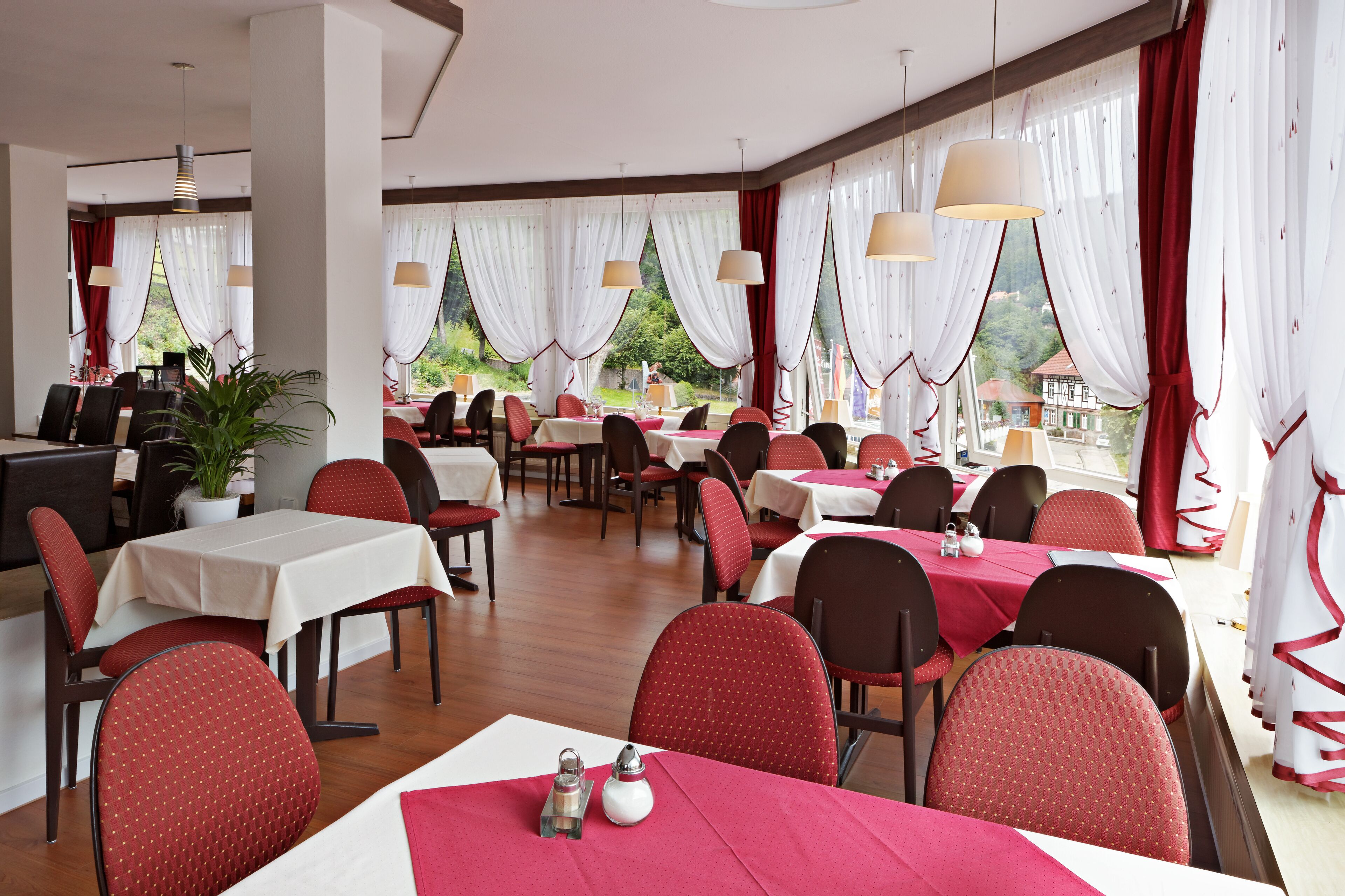 A restaurant with tables set for dining, chairs, and hanging pendant lights.