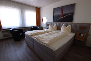 Une chambre d’hôtel avec un grand lit, un bureau, une chaise, une fenêtre avec des rideaux et un tableau représentant un pont.