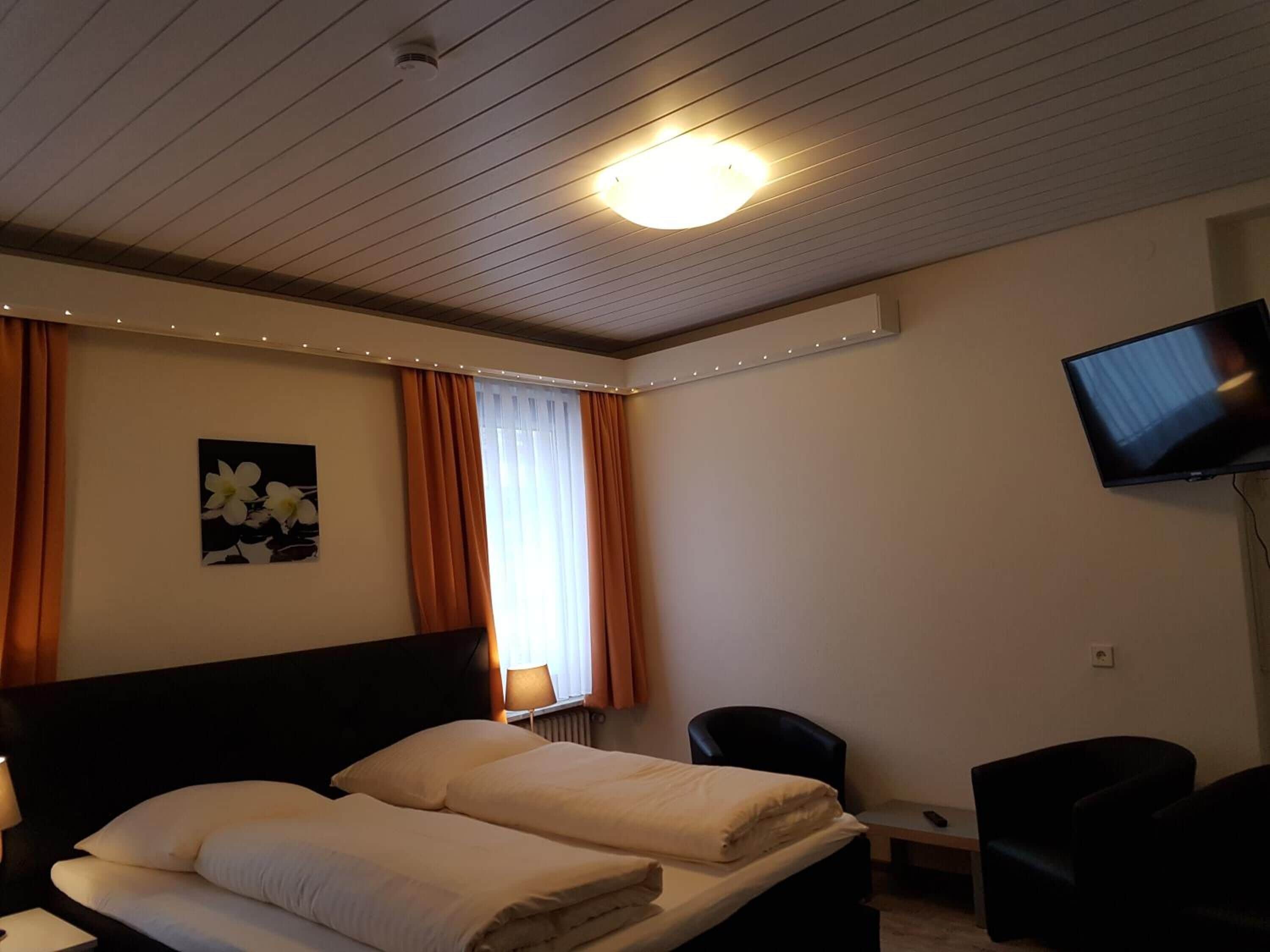 A hotel room with a bed, two chairs, a TV, and a window with curtains.