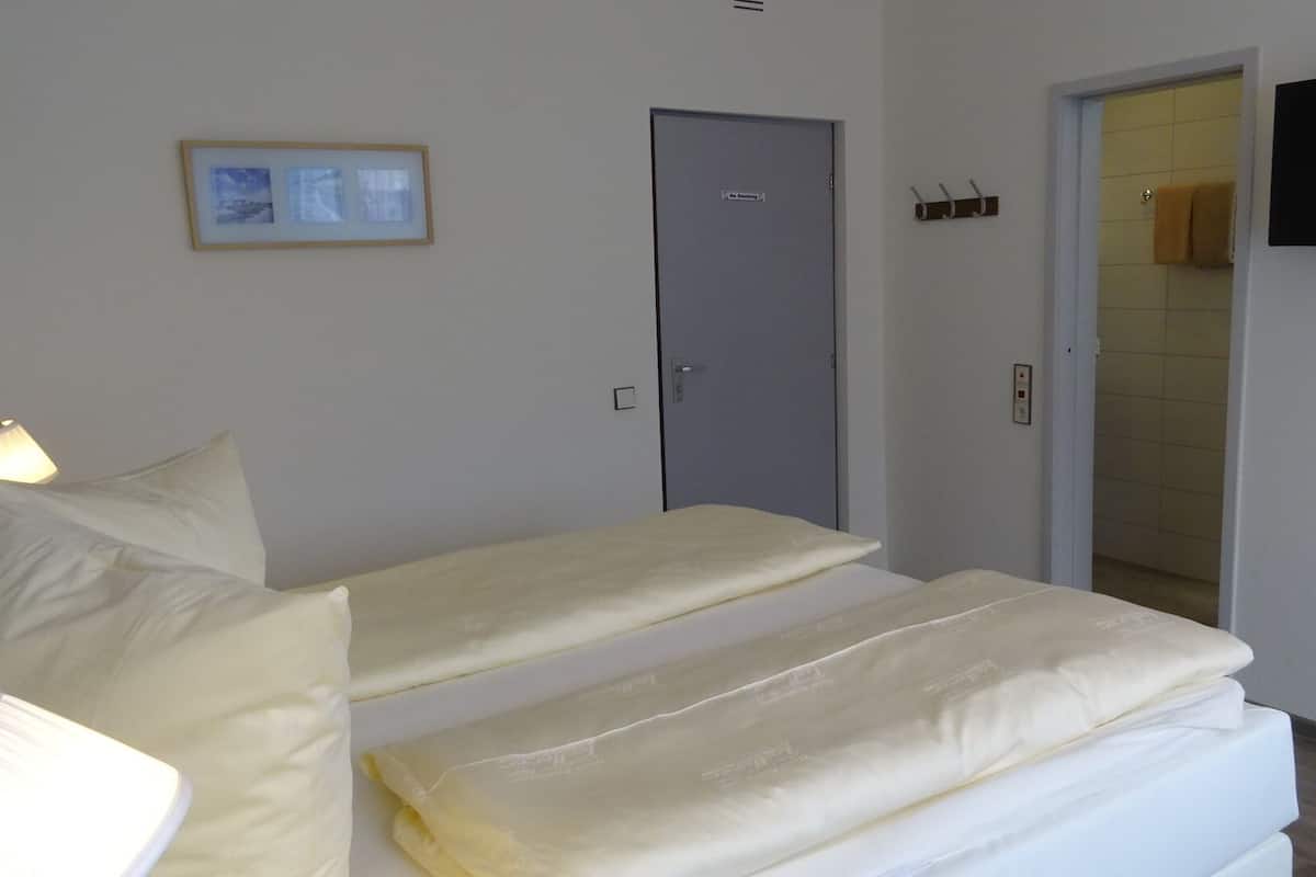 A hotel room with two beds, a television mounted on the wall, and a door leading to a bathroom.