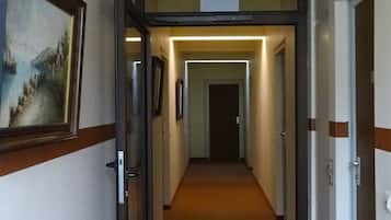 A hotel corridor with a green emergency exit sign, framed artwork on the left, and doors on both sides.