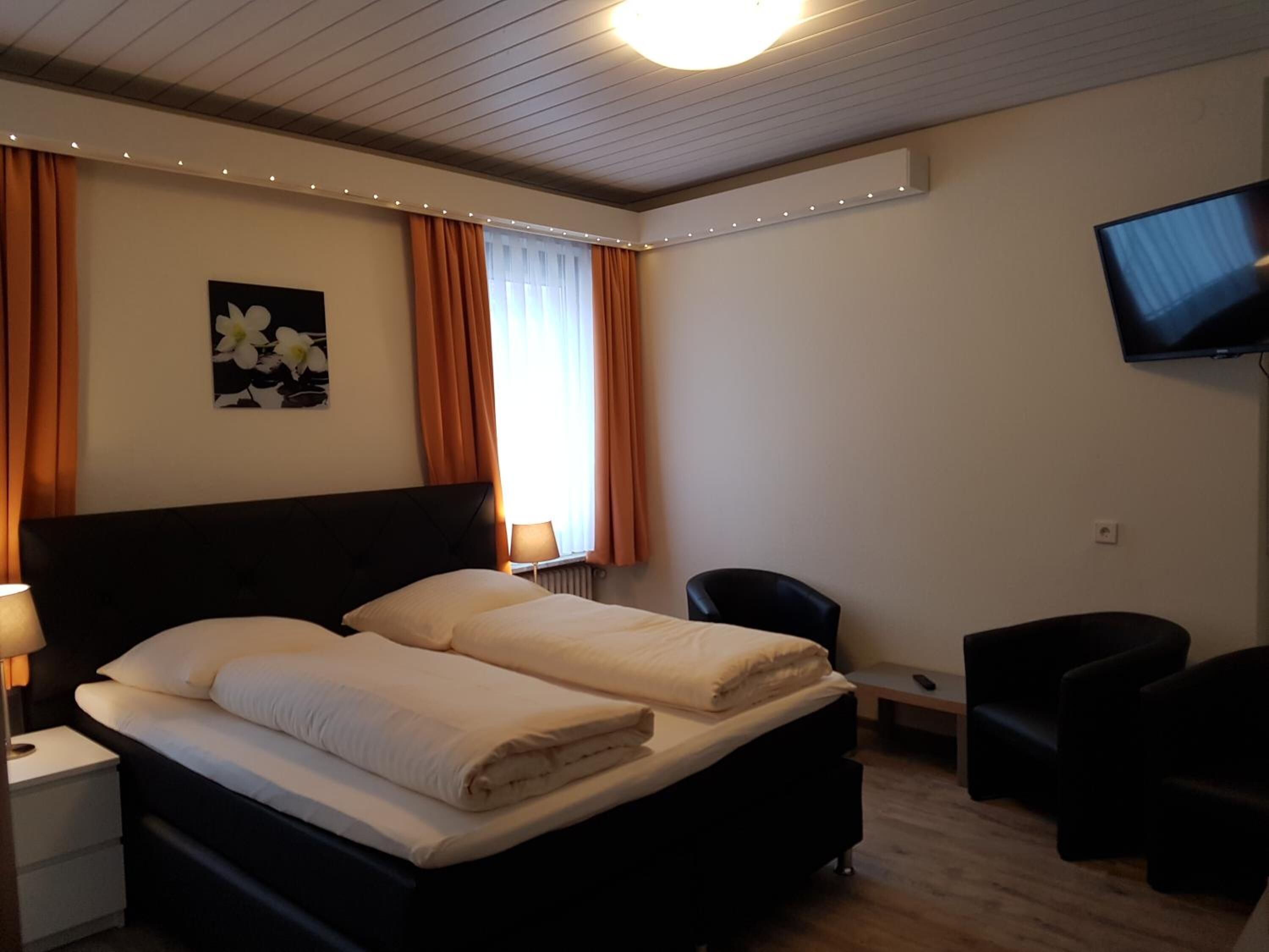 Une chambre d’hôtel avec un lit double, un bureau, une chaise, une télévision et une fenêtre avec des rideaux.