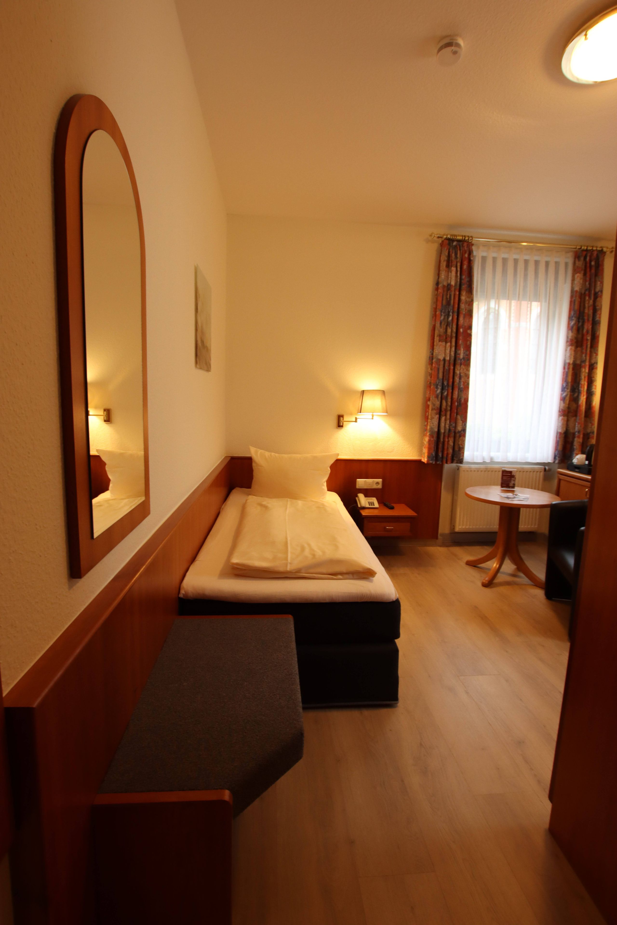 Habitación de hotel compacta con cama, banqueta, mesita, silla y escritorio.