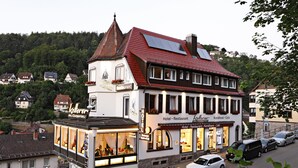 A hotel with a restaurant and cafe, featuring a traditional European architectural style with a red-tiled roof and a tower with a pointed roof.