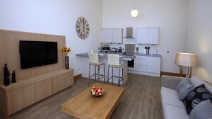 Ein modernes Wohnzimmer mit Flachbildfernseher, einem Couchtisch mit Äpfeln, einer Couch und einer Küchenzeile mit Barhocker.