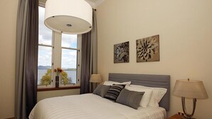 Ein Schlafzimmer mit Bett, Nachttischlampen, einem Nachttisch und einem Fenster mit Vorhängen.