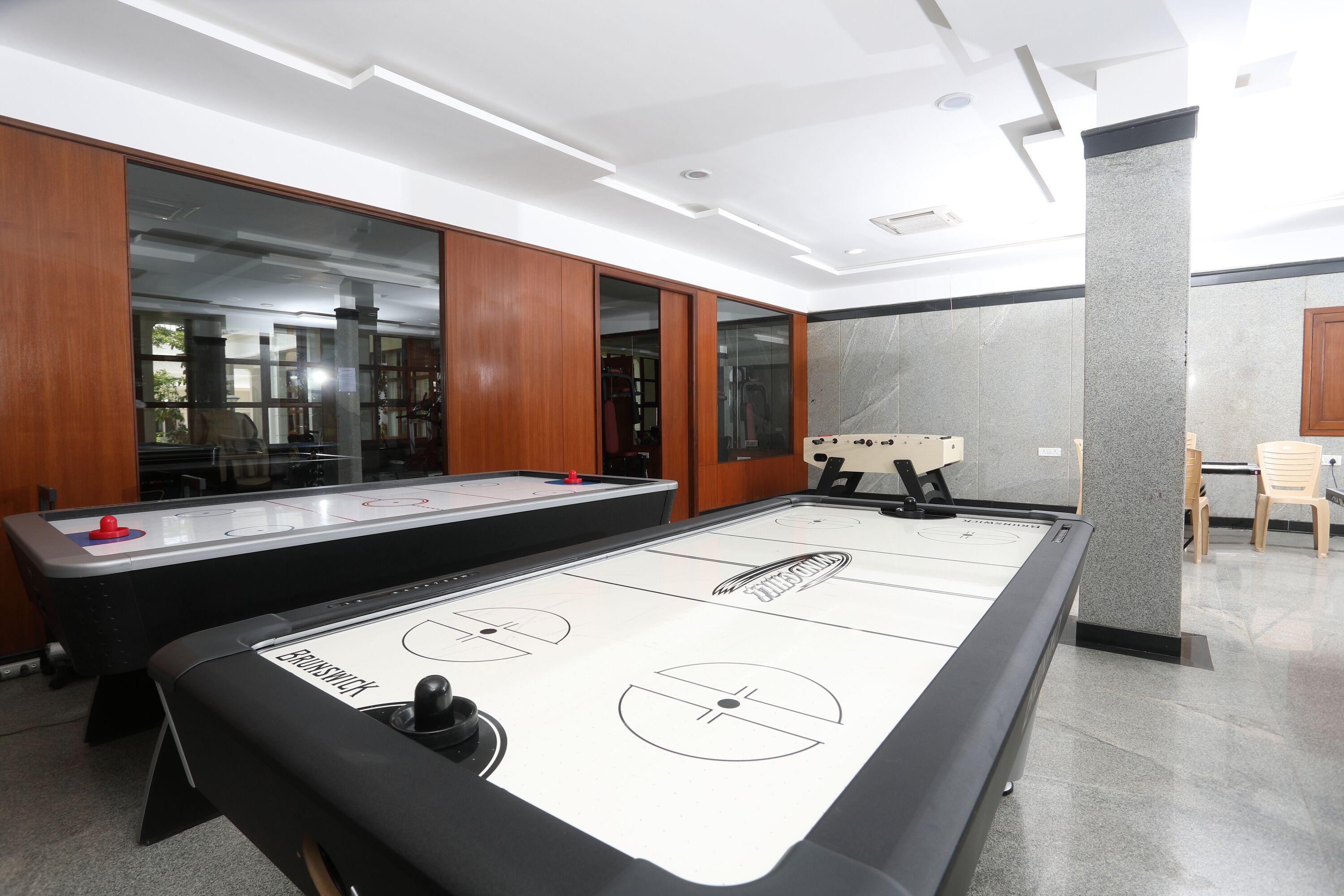 A room with a shuffleboard table, wooden cabinets, and a seating area with chairs.