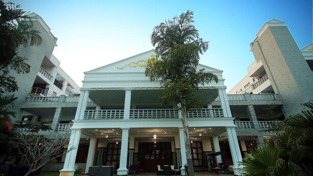 A hotel with a central entrance, multiple balconies, and a well-maintained lawn. - Holiday Valley Nature Resorts (Denkanikota)