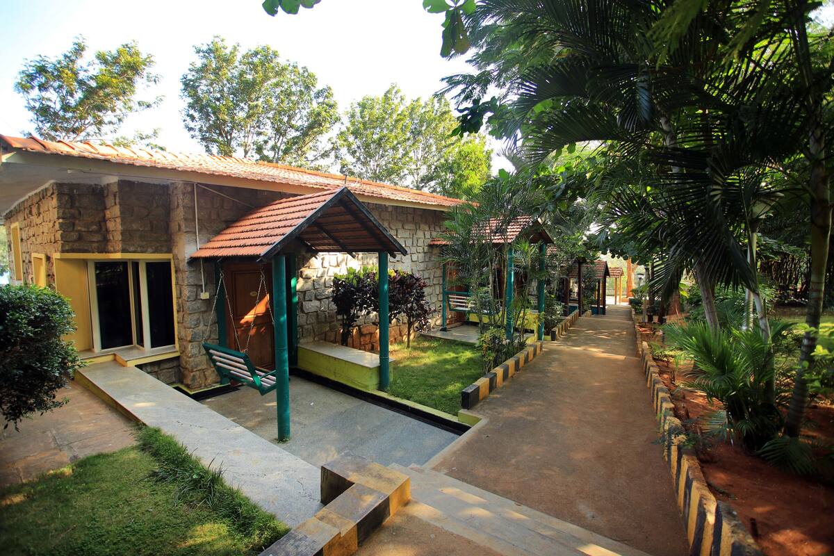 A stone building with a tiled roof, a covered seating area, and a pathway lined with plants.
