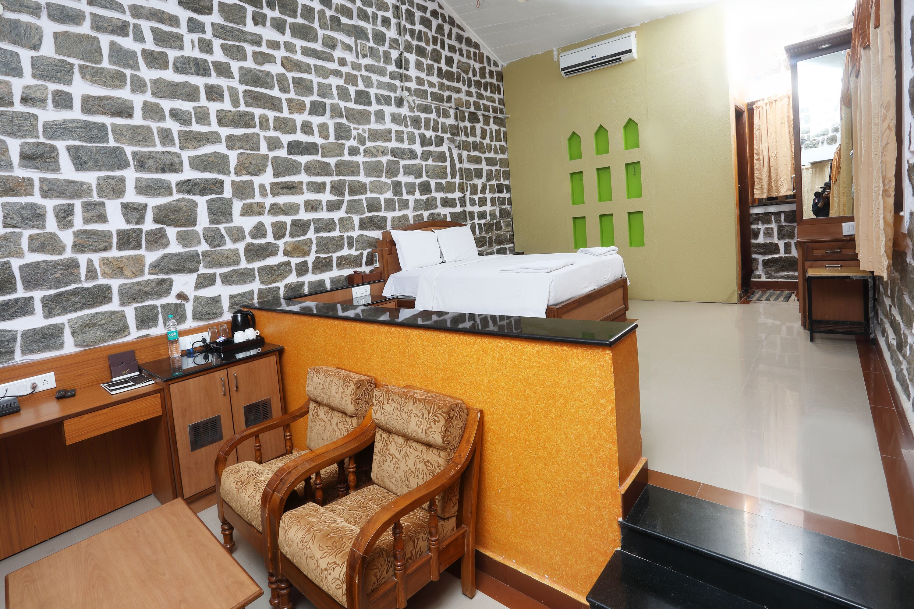 A room with a stone wall, a bed, a desk, and two chairs.