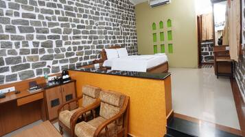 A room with a stone wall, a bed, a desk, and two chairs.