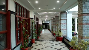 A corridor with tiled flooring, potted plants, and red-framed windows. - Holiday Valley Nature Resorts (Denkanikota)